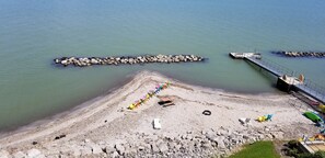 Ein Strand mit felsigem Ufer, einer Seebrücke und bunten Liegestühlen.