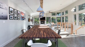 A spacious dining area with a long wooden table, white chairs, and a view of the outdoors through large windows. - Dream Views & Chef's Kitchen-Modern, Mountain Home w/ Hot Tub (Anchorage)