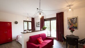 Un espacio habitable moderno con un sofá rojo, una mesa de comedor con sillas, un armario rojo y una ventana con cortinas.