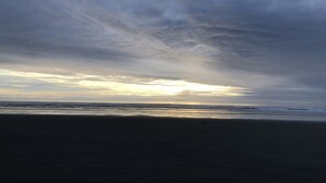 Ein Strand mit bewölktem Himmel und der Sonne, die am oder über dem Horizont untergeht oder aufgeht.