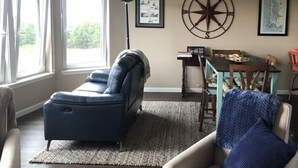 Ein Wohnzimmer mit einem dunkelblauen Sofa, einem Esstisch mit Stühlen, einem großen Fenster und einer Wanddekoration in Form eines Kompasses.