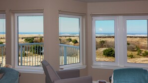 Ein Zimmer mit drei großen Fenstern und Blick auf Strand und Dünen.