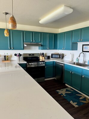 Una cocina con armarios verde mar, una encimera blanca, una estufa, un microondas y un lavabo.