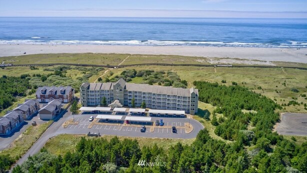 Ein Luftbild eines Hotels mit mehreren Gebäuden, einem Parkplatz und einem Strand im Hintergrund.