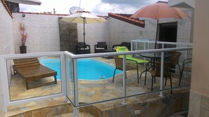 Un espace piscine avec un banc en bois, des chaises d’extérieur et une table.