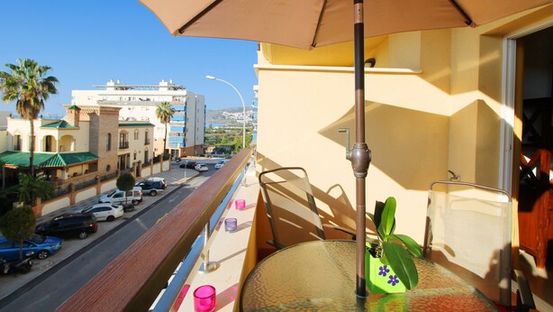 A balcony with a table, chair, umbrella, and a potted plant. - 1081 Apartment Poseidon (Nerja)