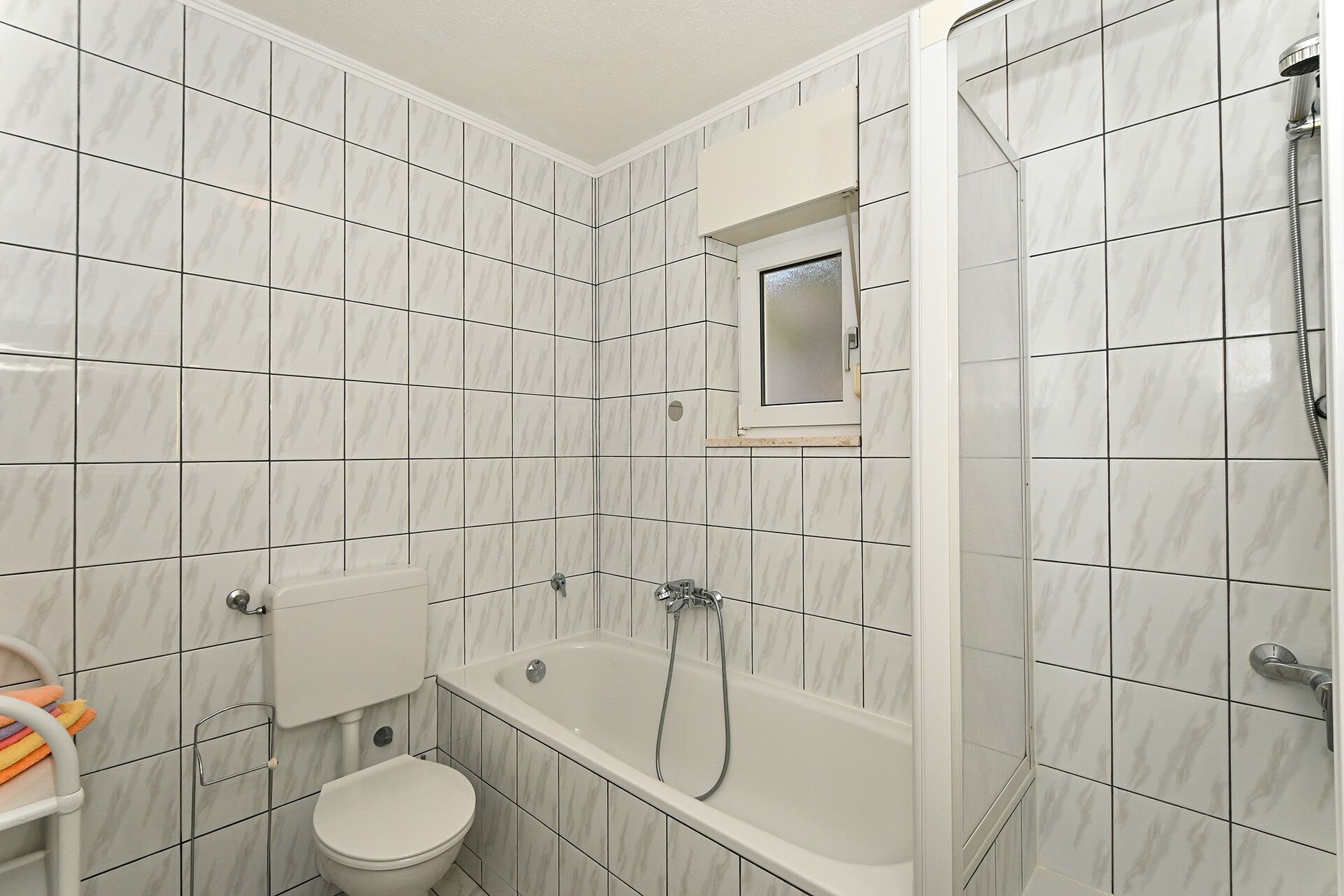 A bathroom with white marble tiles, a bathtub, a toilet, and a shower.