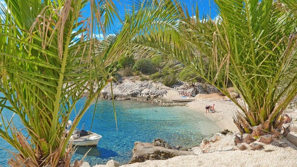 Une plage avec une eau d’un bleu limpide, un bateau et un paysage rocheux.