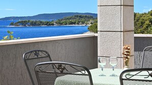 Un balcon avec vue sur la mer, une table avec deux verres et un vase rempli de fleurs séchées.