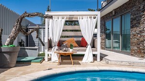 A modern outdoor seating area with a pool, featuring a white canopy, a wooden table, and a sofa with cushions. - Cantua Villa, AC, Wifi, Swimming pool (Azeitão)