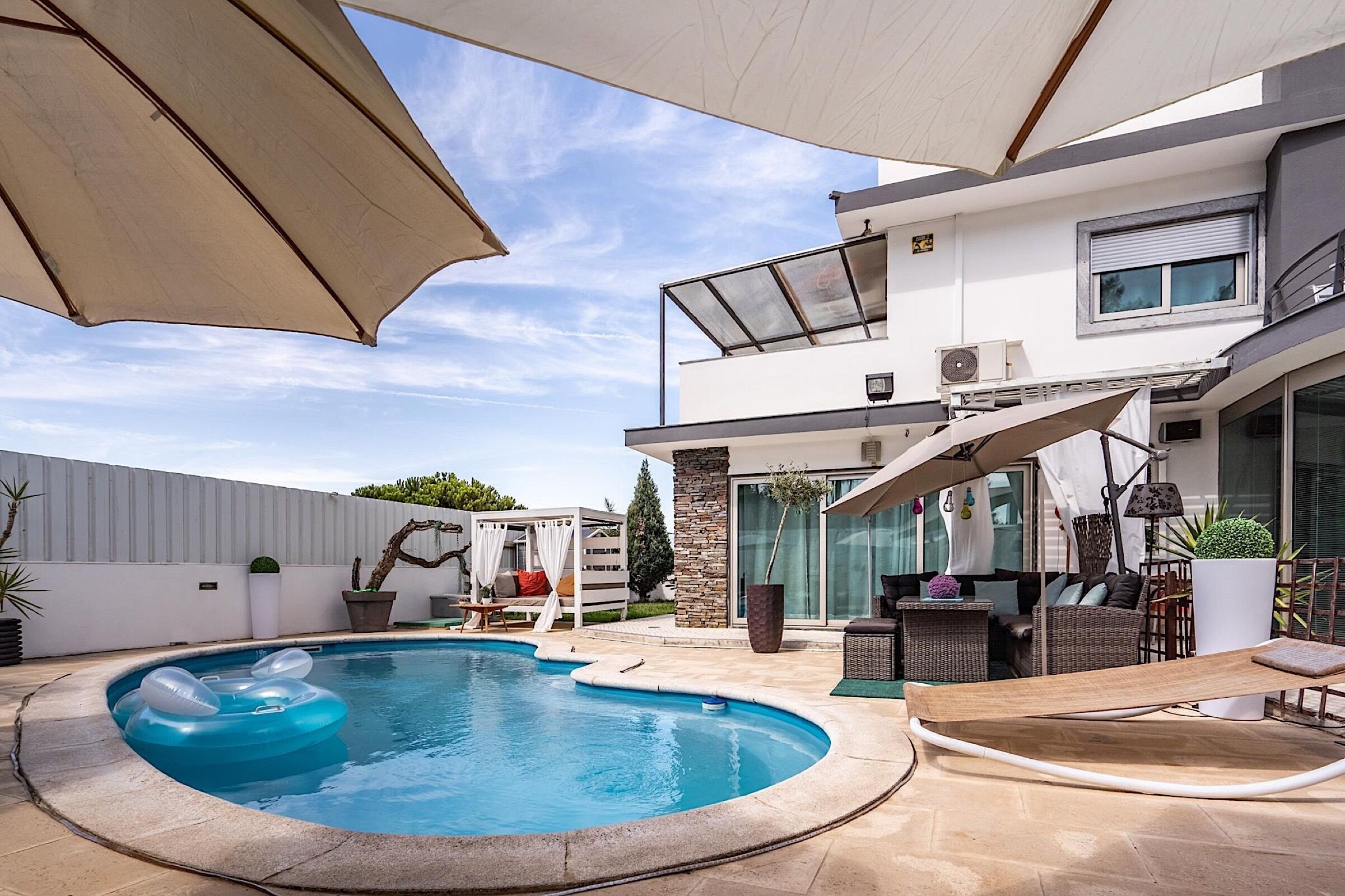 Ein moderner Poolbereich im Freien mit einem kreisförmigen Pool, Liegestühlen und einer überdachten Sitzgruppe.