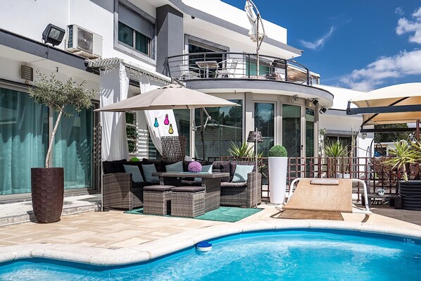 A modern outdoor pool area with wicker furniture, a lounge chair, and a small slide.