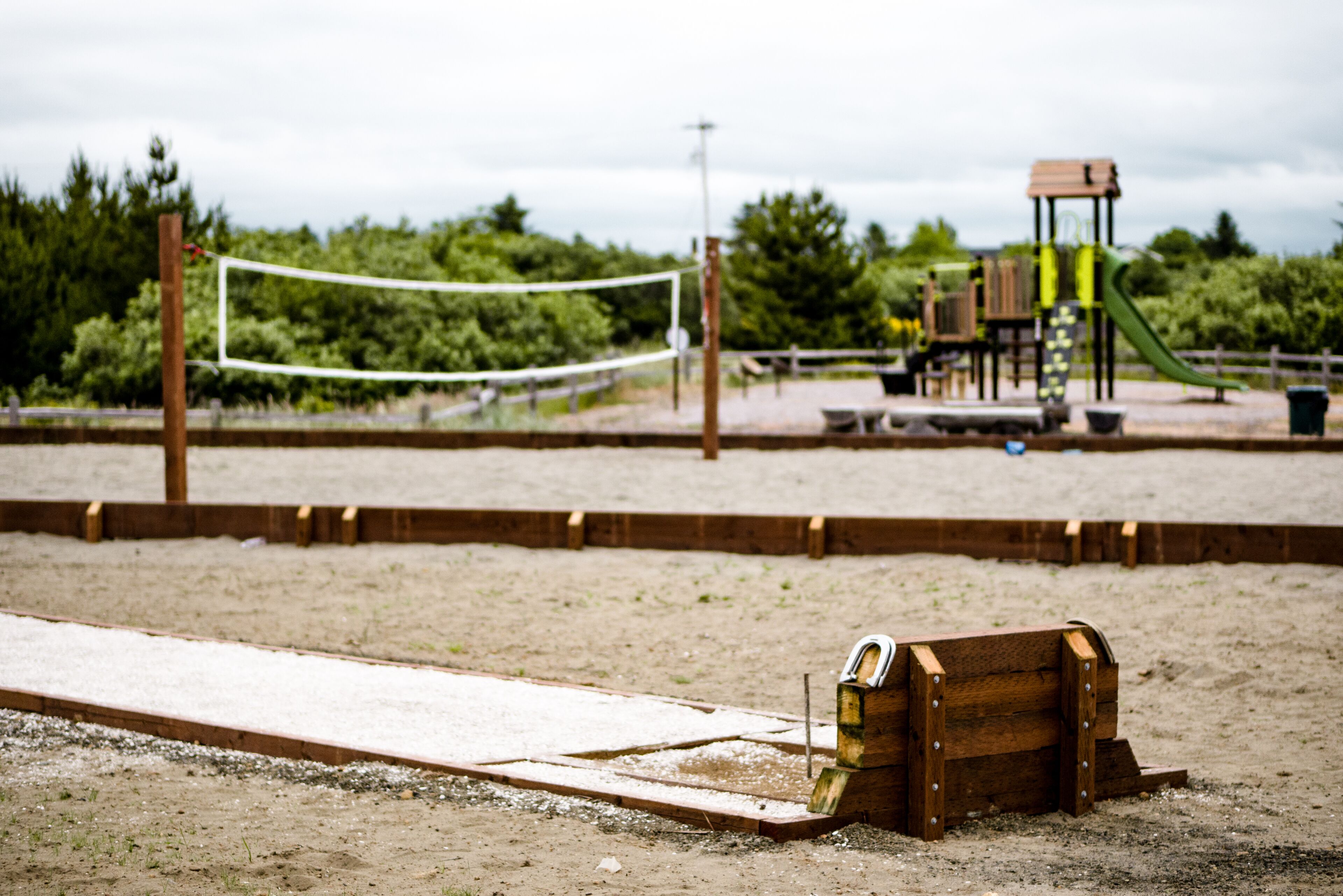 A sandy beach with a volleyball net, wooden play structures, and a slide.