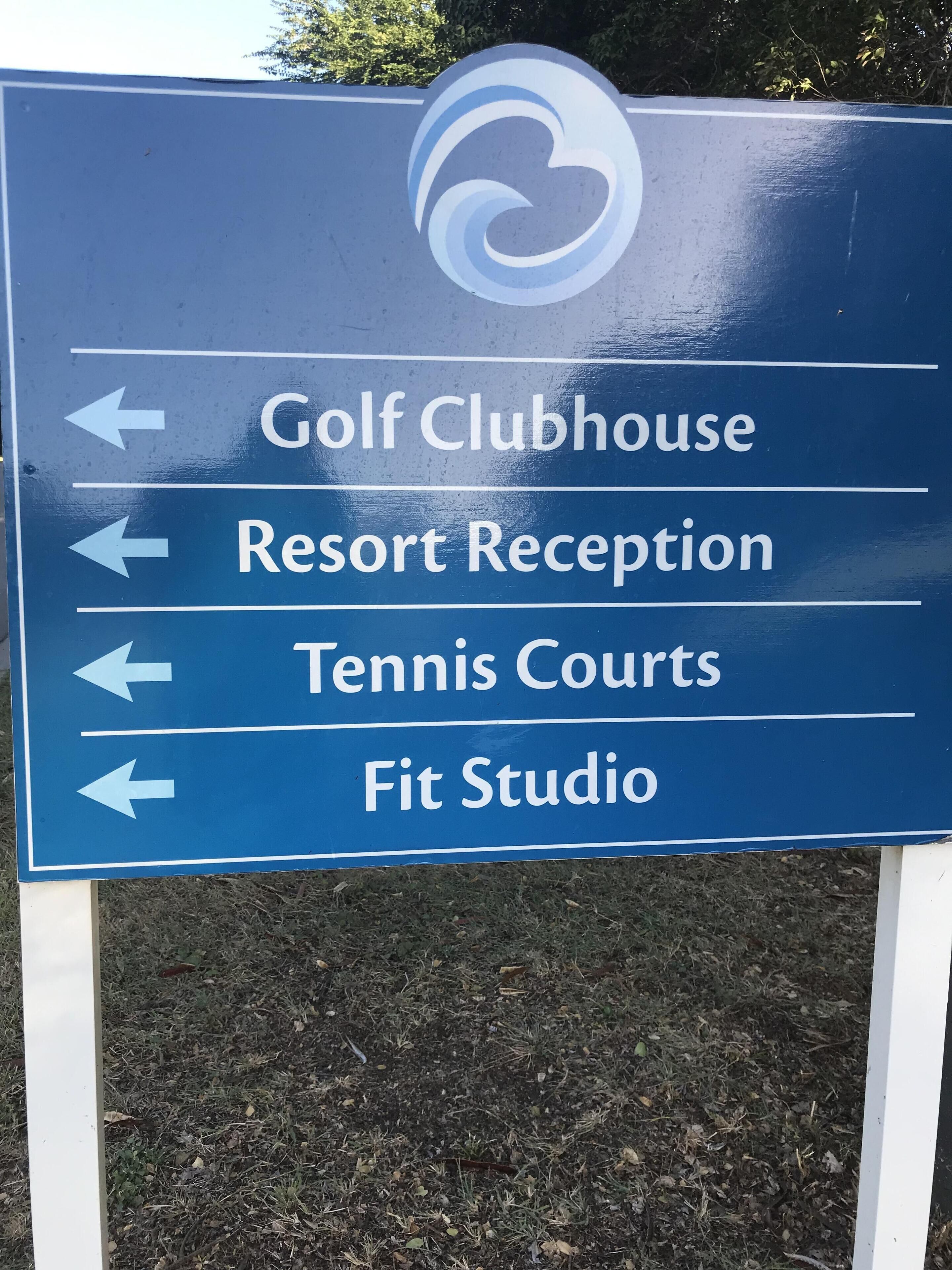 A directional sign with arrows pointing to facilities such as a Golf Clubhouse, Resort Reception, Tennis Courts, and Fit Studio.