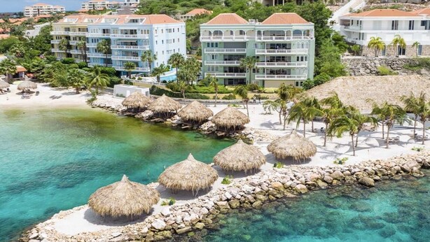 Un resort con propiedades frente al mar, aguas turquesas cristalinas y sombrillas de paja.