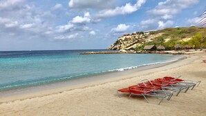 Una playa con agua turquesa cristalina, un acantilado rocoso y sillas de playa rojas.