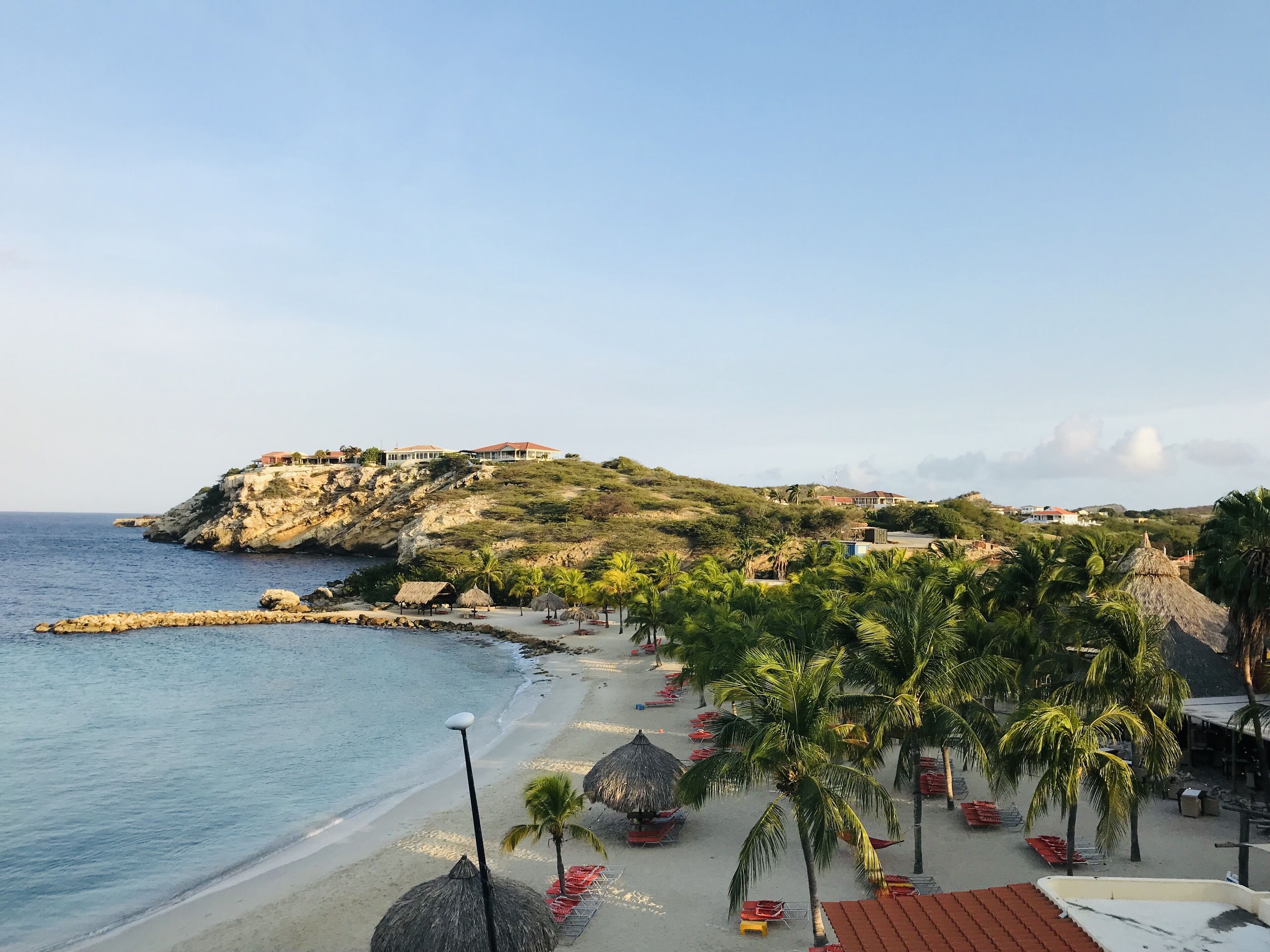Une plage côtière avec un promontoire rocheux, des palmiers et des parasols de plage.