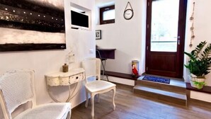 A room with a wooden floor, a white chair, a small table, a television, a clock, and a door with a mat. - Self catering Residence Masnaiot for 2 people (Cossano Belbo)