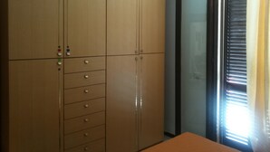 Ein Zimmer mit großem Kleiderschrank, einer Schiebetür aus Glas und einem Fenster mit Jalousien.