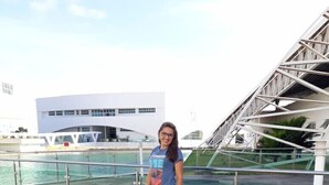 A woman standing by a waterfront with a modern building and a bridge in the background. - Pousada Refúgio (João Pessoa)