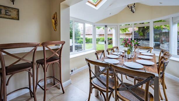 A dining area with a high ceiling, skylight, and large windows offering a view of the garden. - The Old Manor House, Brancaster, Norfolk (King's Lynn)