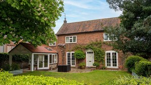 A brick house with a tiled roof, a covered patio, and a well-maintained garden. - The Old Manor House, Brancaster, Norfolk (King's Lynn)