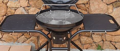 Una parrilla portátil con estructura metálica y ruedas, ubicada en un patio con baldosas.