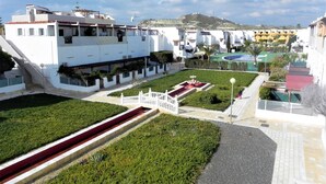 Une cour avec une fontaine, un bâtiment blanc doté de balcons, et une vue sur une colline en arrière-plan.
