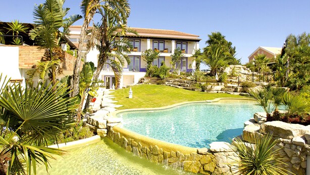 Una piscina rodeada de palmeras y un edificio con varios balcones.