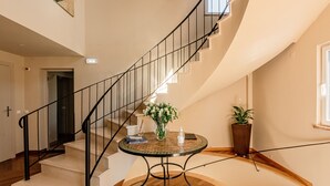 Una escalera con barandilla negra, una mesa redonda con un jarrón de flores y una planta en maceta en la plataforma.