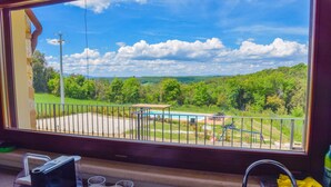 Blick aus einem Fenster mit Balkon, Pool und grüner Landschaft.