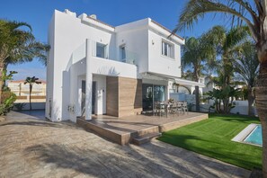 Une maison moderne à deux étages, dotée d’un patio, d’une piscine et d’une pelouse bien entretenue.