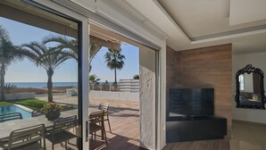 Un salon moderne doté d’un téléviseur, d’un mur recouvert de panneaux en bois et d’une porte vitrée donnant sur un espace piscine aménagé avec du mobilier d’extérieur.