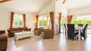 A spacious living room with a high ceiling, a dining area with a table and chairs, and large windows with curtains. - Villa Lune for 10 people with private pool (Vallon Pont D'Arc)