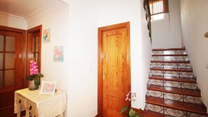 Una escalera de madera con azulejos decorativos, una puerta de madera y una pequeña mesa con un florero y un marco de fotos.