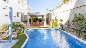 Una piscina con borde de azulejos, un porche cubierto y una pared de piedra con vegetación.