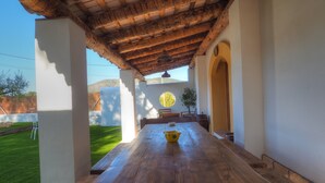 An outdoor dining area with a wooden table, a yellow bowl, and a view of a garden and mountains in the background. - Villa Can Roig by Hello Homes Sitges (Sitges)