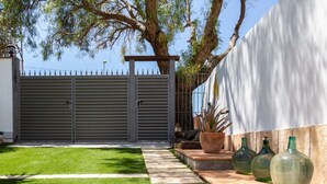 A gated backyard with a well-maintained lawn, a stone pathway, and decorative planters. - Villa Can Roig by Hello Homes Sitges (Sitges)