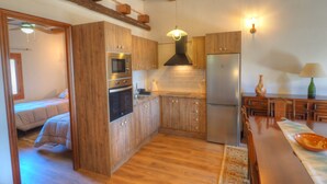 A compact kitchen with wooden cabinets, a built-in oven, microwave, and refrigerator. There is a dining area with a table and chairs. - Villa Can Roig by Hello Homes Sitges (Sitges)
