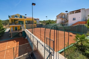 Un court de tennis avec un filet, entouré de bâtiments et un escalier menant à un balcon.
