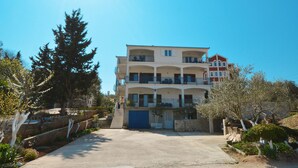 A multi-story building with balconies, a driveway, and surrounding vegetation. - BLUEHOUSE 2, cozy apartment for 4 persons, 250m from a pebble beach (Okrug Gornji)
