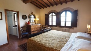 A bedroom with a large bed, wooden dresser, two chairs, a mirror, and two windows with shutters. - Casa Acacia, an ancient tower nestled in the green hills of San Giminiano (San Gimignano)