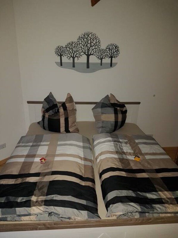 Un lit double avec une literie à rayures et deux oreillers, une tête de lit en bois et une décoration murale représentant des arbres.