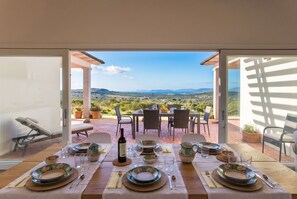 An outdoor dining area with a table set for four, a view of the countryside, and a pergola structure.