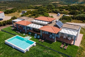 Una casa grande con piscina, varias habitaciones con techos de tejas y un área de estar cubierta al aire libre.