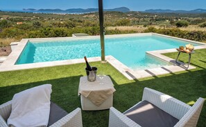 A pool with a view of the countryside, a bottle of champagne, and a table with snacks.