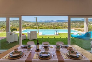 A dining table set with plates, glasses, and cutlery, overlooking a pool and lush landscape. - Alghero Spectacular Villa Carrabufas sea view  near the centre (Alghero)