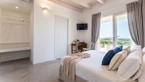 Ein Schlafzimmer mit Bett, Schreibtisch, Fernseher und Blick ins Freie.