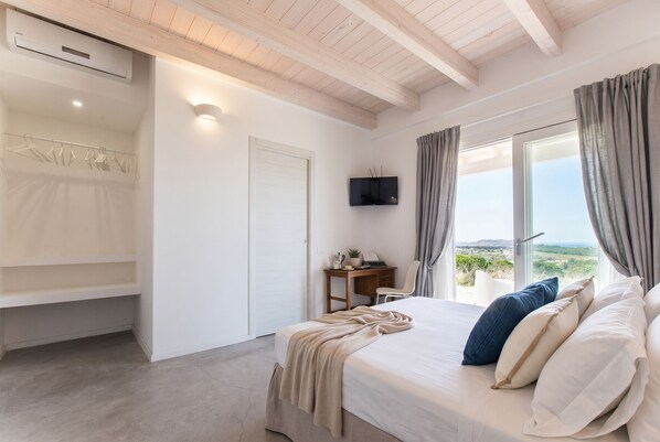 Un dormitorio con cama, escritorio, televisor y vistas al exterior.