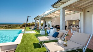 Ein Poolbereich mit Liegestühlen, einer Pergola und Blick aufs Meer.
